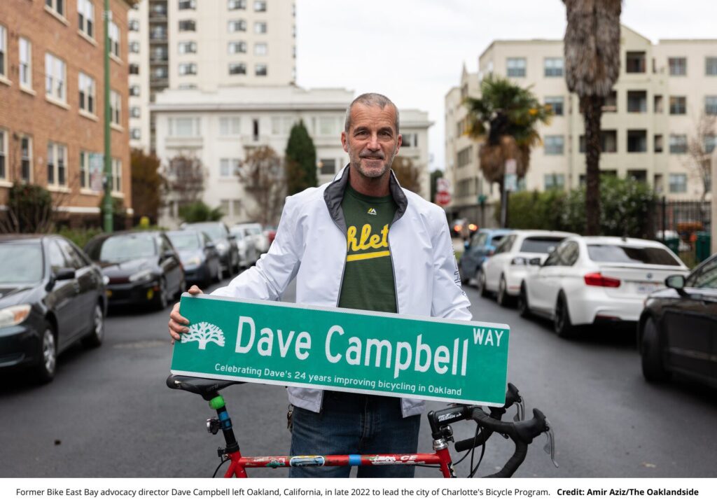 Dave Campbell holding a "Dave Campbell Way" sign in Oakland, CA